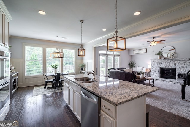 kitchen featuring a kitchen island with sink, sink, stainless steel dishwasher, and hanging light fixtures