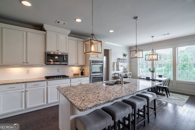 kitchen with sink, appliances with stainless steel finishes, white cabinetry, a kitchen breakfast bar, and an island with sink