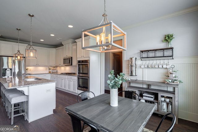 kitchen with a kitchen island with sink, stainless steel appliances, light stone counters, dark hardwood / wood-style flooring, and decorative light fixtures