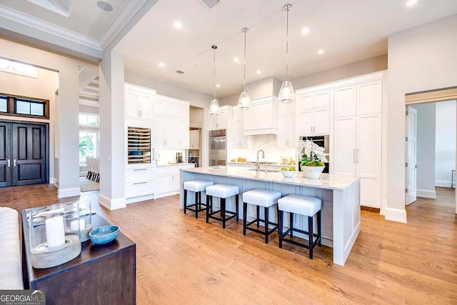 kitchen with a breakfast bar area, light countertops, white cabinetry, light wood-type flooring, and built in refrigerator