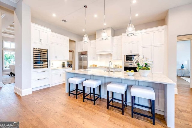 kitchen featuring built in fridge, white cabinets, light wood-style flooring, and a breakfast bar area