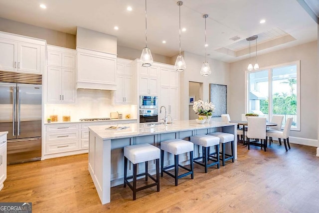 kitchen with a breakfast bar area, a sink, white cabinets, appliances with stainless steel finishes, and light wood-type flooring