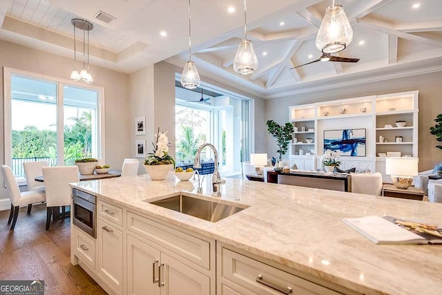 kitchen with light stone counters, stainless steel microwave, wood finished floors, hanging light fixtures, and a sink