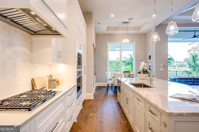 kitchen featuring custom exhaust hood, a raised ceiling, stainless steel gas stovetop, white cabinetry, and a sink