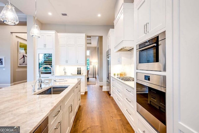 kitchen featuring a sink, visible vents, white cabinets, light wood-type flooring, and decorative light fixtures