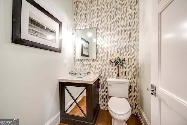 half bath with baseboards, vanity, and toilet