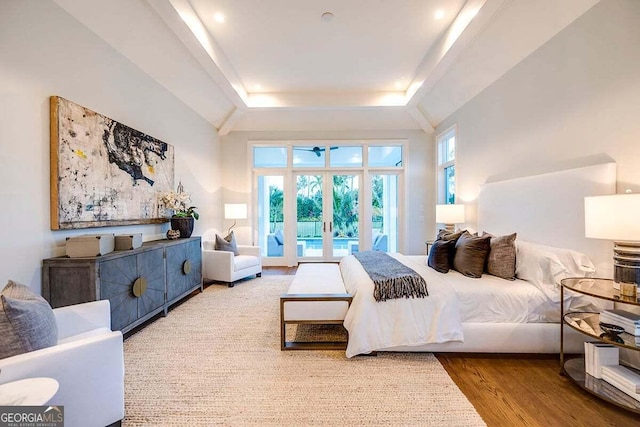 bedroom with multiple windows, a raised ceiling, wood finished floors, and french doors