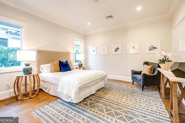 bedroom featuring baseboards, wood finished floors, visible vents, and crown molding