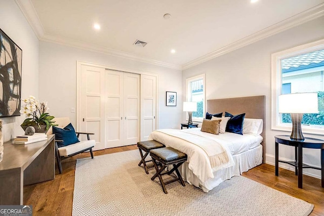 bedroom with a closet, wood finished floors, visible vents, and crown molding