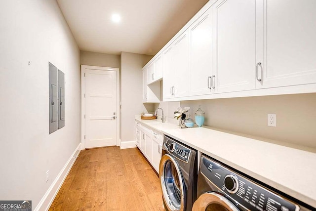 clothes washing area featuring cabinet space, baseboards, washer and clothes dryer, light wood-style flooring, and a sink