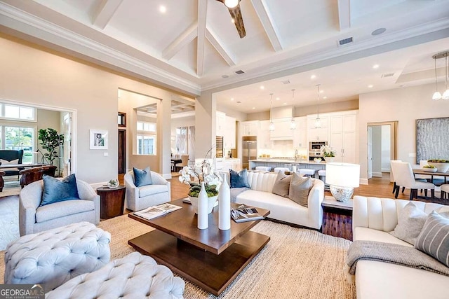 living room featuring light wood-style floors, beam ceiling, visible vents, and a towering ceiling