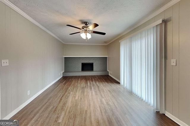 unfurnished living room with ceiling fan, a fireplace, wood-type flooring, ornamental molding, and a textured ceiling