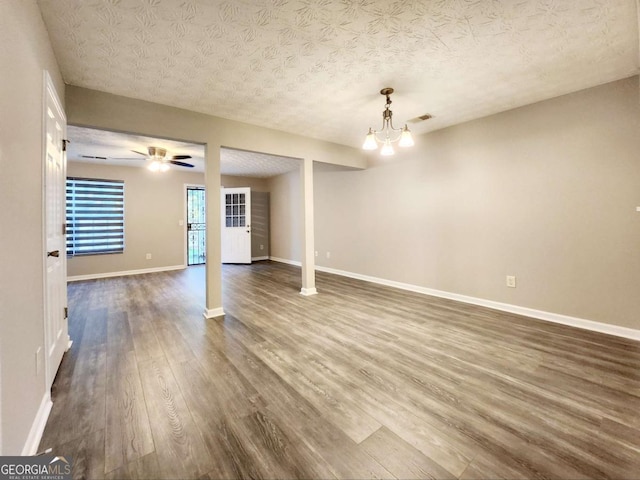 empty room with ceiling fan with notable chandelier, dark hardwood / wood-style floors, and a textured ceiling