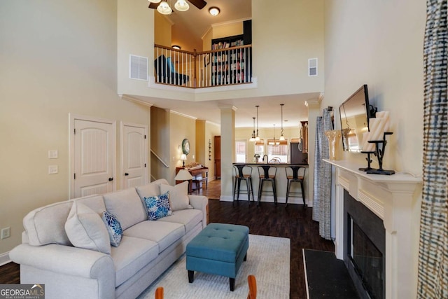 living room with crown molding, decorative columns, dark hardwood / wood-style floors, and ceiling fan