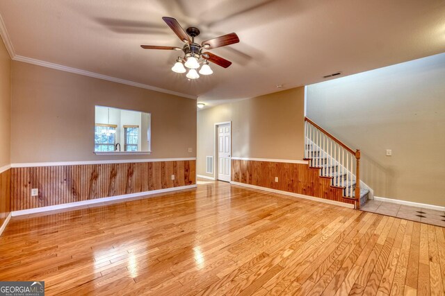 empty room featuring ceiling fan, ornamental molding, wood walls, and light wood-type flooring