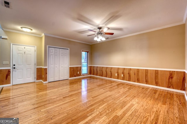 spare room featuring ceiling fan, ornamental molding, wooden walls, and light hardwood / wood-style floors