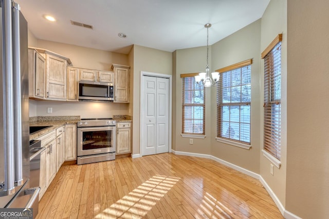 kitchen with pendant lighting, appliances with stainless steel finishes, light stone counters, light brown cabinetry, and light wood-type flooring