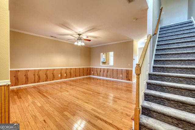 interior space with hardwood / wood-style flooring, ornamental molding, ceiling fan, and wood walls