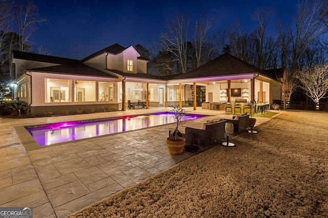 pool at twilight with area for grilling, a patio, ceiling fan, and exterior bar