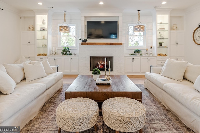 living room featuring crown molding, wood-type flooring, and a brick fireplace