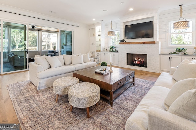 living room featuring a brick fireplace, wood-type flooring, ornamental molding, and a healthy amount of sunlight