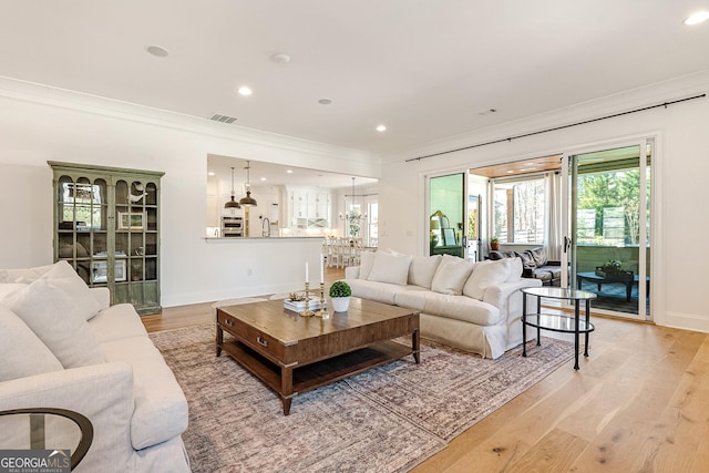 living room with crown molding, light hardwood / wood-style floors, and a chandelier