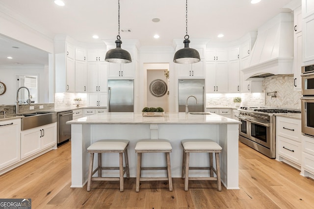 kitchen featuring sink, high end appliances, light stone counters, a center island with sink, and custom exhaust hood