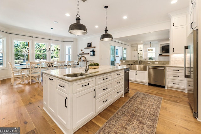 kitchen featuring sink, appliances with stainless steel finishes, a kitchen island with sink, white cabinetry, and hanging light fixtures