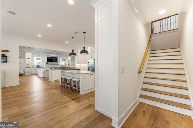 staircase featuring sink, crown molding, and wood-type flooring