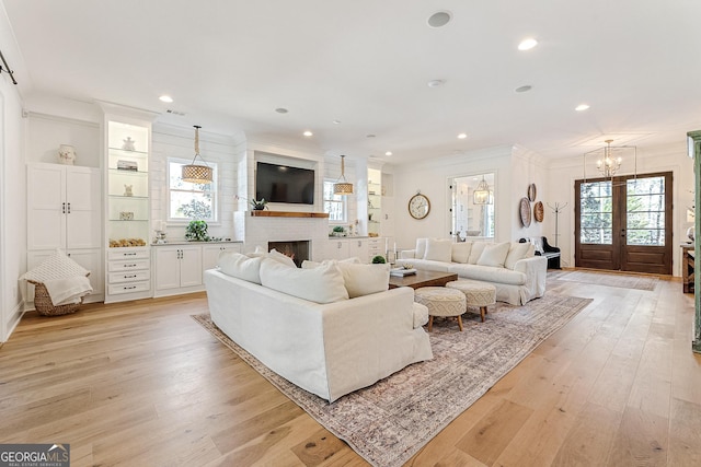 living room featuring a fireplace, ornamental molding, light hardwood / wood-style floors, and french doors