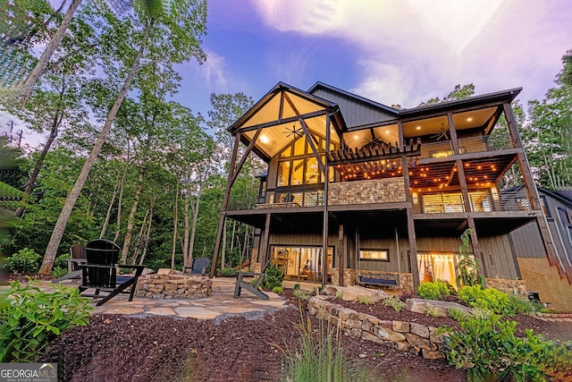 back house at dusk with ceiling fan, a balcony, and a patio