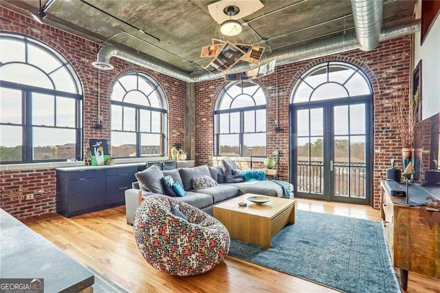 living area with brick wall, light wood-type flooring, and a high ceiling