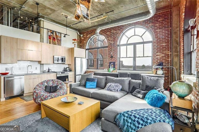 living area featuring brick wall, a high ceiling, and light wood-style floors