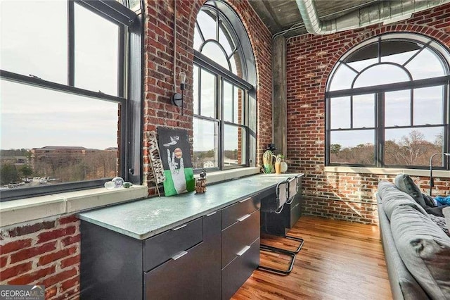 office featuring wood finished floors, a high ceiling, a healthy amount of sunlight, and brick wall