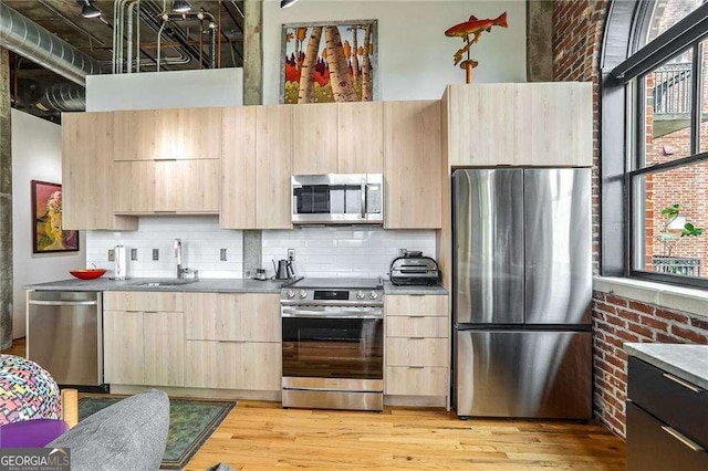 kitchen with appliances with stainless steel finishes, light brown cabinets, brick wall, and a sink