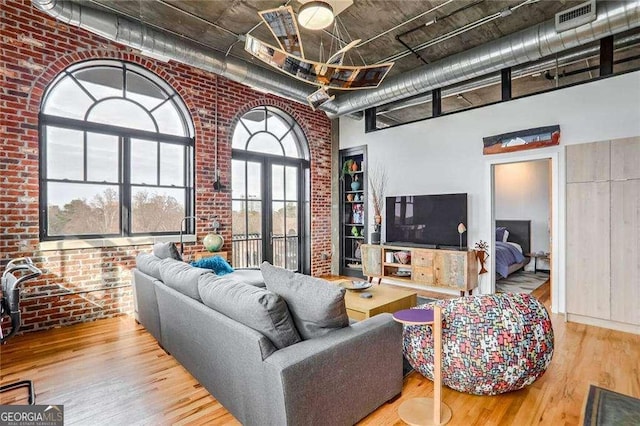 living room with visible vents, wood finished floors, a towering ceiling, and brick wall