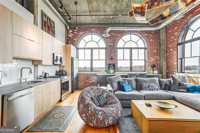 living room with a high ceiling, light wood-style floors, and brick wall