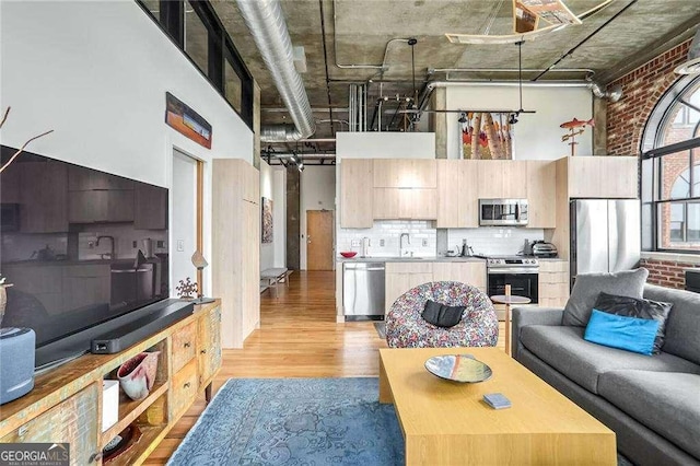 living area with light wood finished floors, brick wall, and a towering ceiling