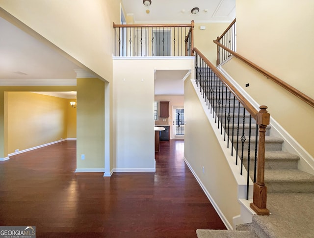 stairway featuring ornamental molding, a towering ceiling, and hardwood / wood-style floors