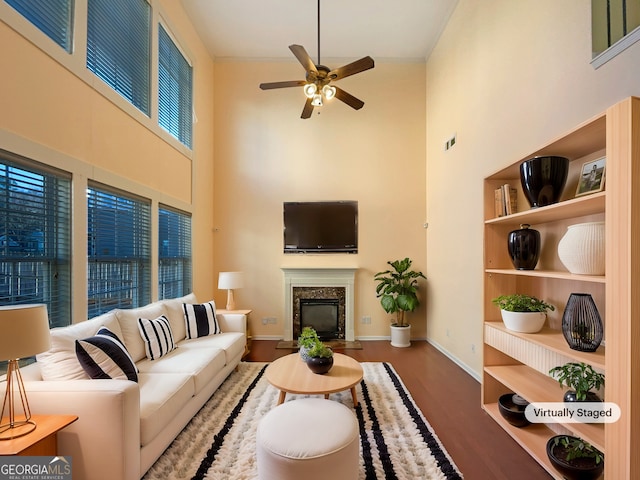 living room featuring a premium fireplace, a towering ceiling, hardwood / wood-style floors, and ceiling fan