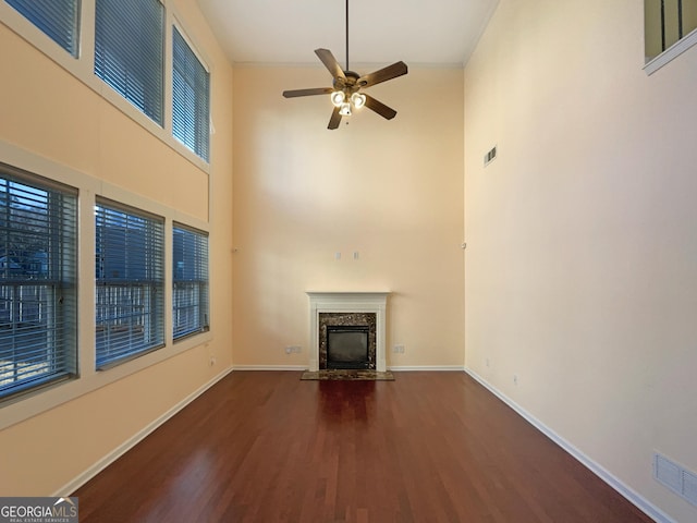 unfurnished living room featuring dark hardwood / wood-style flooring, a fireplace, ceiling fan, and a high ceiling