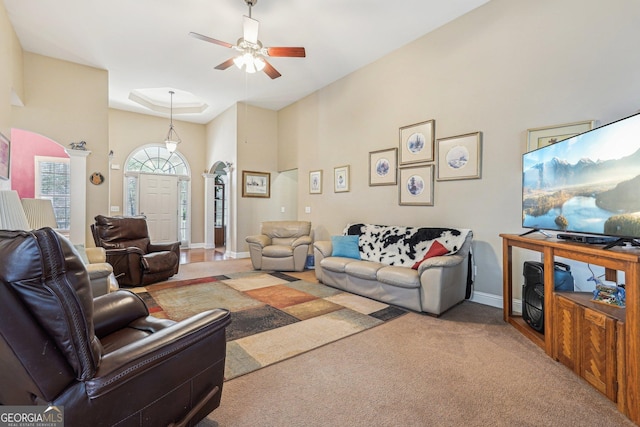 living room with arched walkways, light colored carpet, baseboards, ceiling fan, and ornate columns