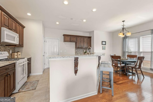 kitchen featuring decorative light fixtures, tasteful backsplash, a kitchen bar, light stone counters, and white appliances