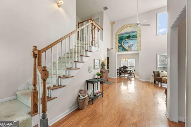 staircase with hardwood / wood-style flooring, ceiling fan with notable chandelier, and a towering ceiling