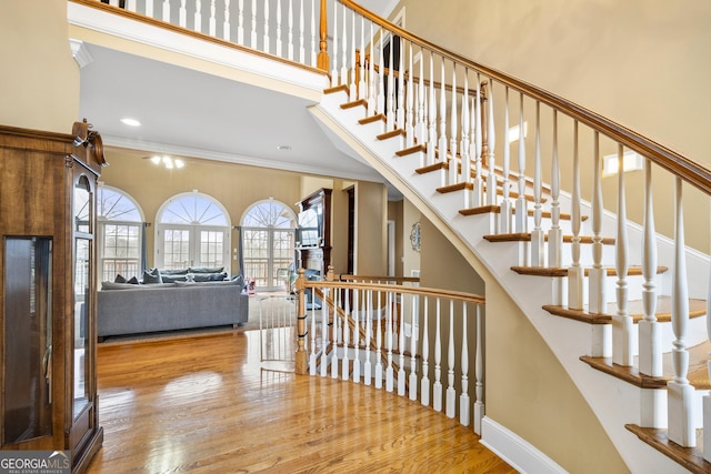 staircase featuring hardwood / wood-style flooring, a towering ceiling, ornamental molding, and a wealth of natural light