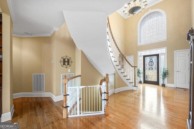 foyer featuring a high ceiling, ornamental molding, hardwood / wood-style floors, and a notable chandelier