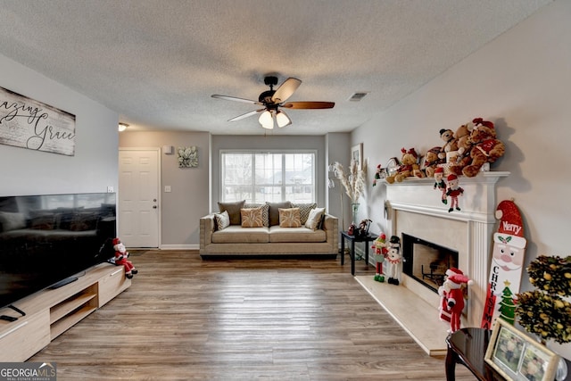 living room featuring a premium fireplace, hardwood / wood-style floors, a textured ceiling, and ceiling fan