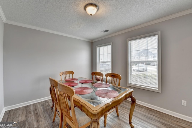 dining area featuring hardwood / wood-style flooring, ornamental molding, and a textured ceiling