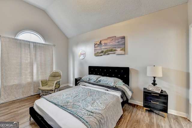 bedroom with vaulted ceiling, a textured ceiling, and light hardwood / wood-style flooring