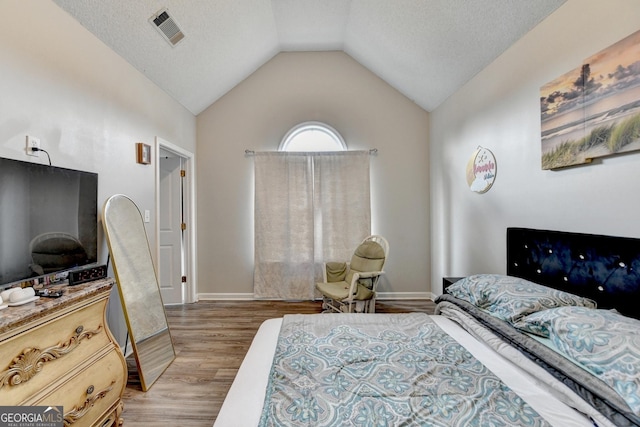 bedroom with hardwood / wood-style flooring, vaulted ceiling, and a textured ceiling